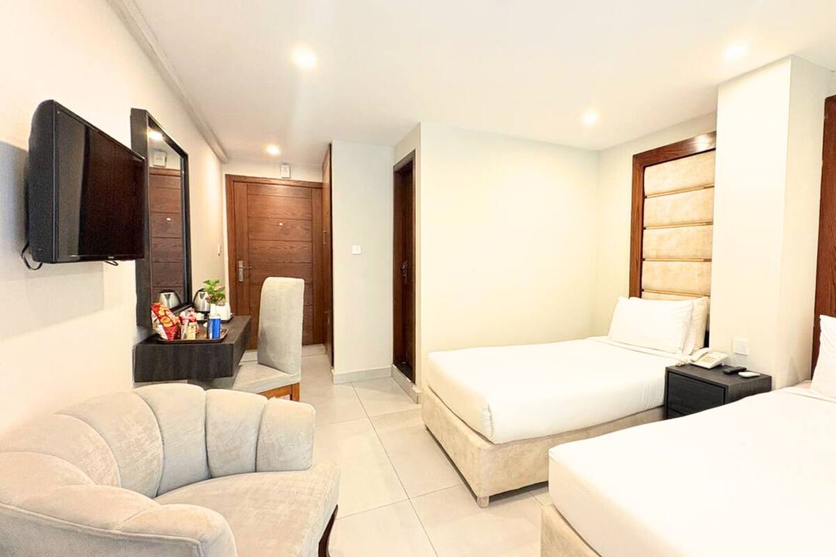 A hotel room with two beds, a TV, a chair, and a small table with snacks.