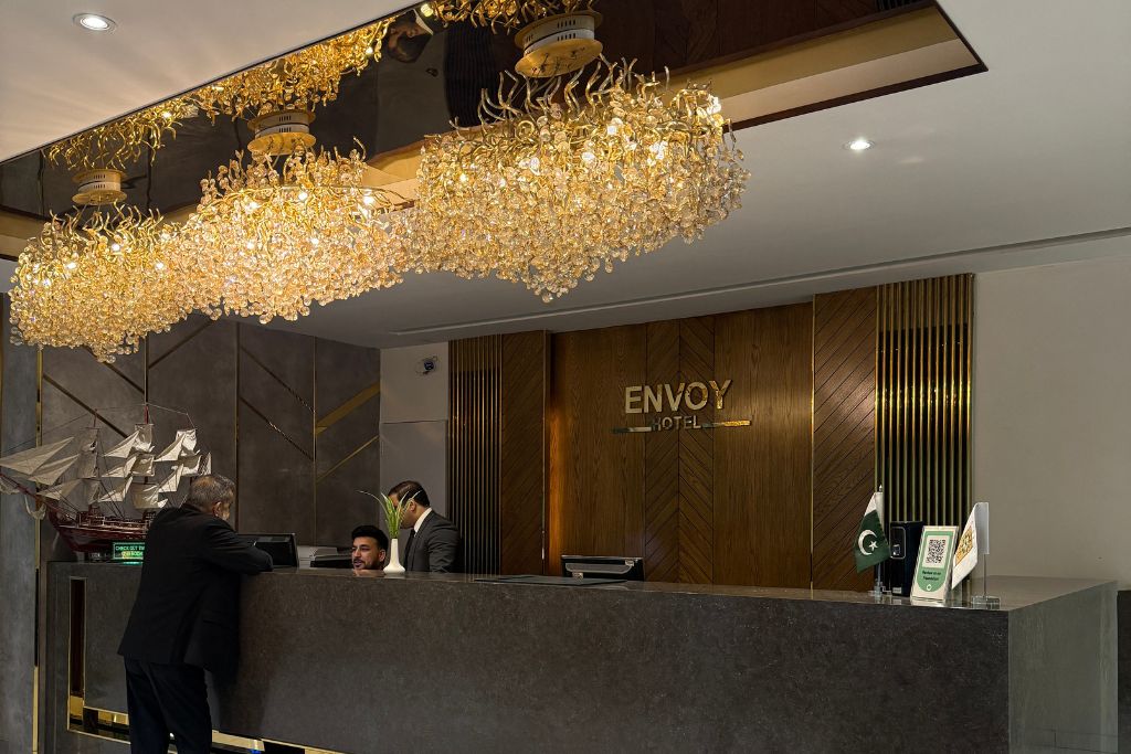 Ein Hotelrezeptionstresen mit einer Chandelüster, ein Holzboden im Empfangsbereich und ein Schild mit der Aufschrift 'ENVOY HOTEL'.
