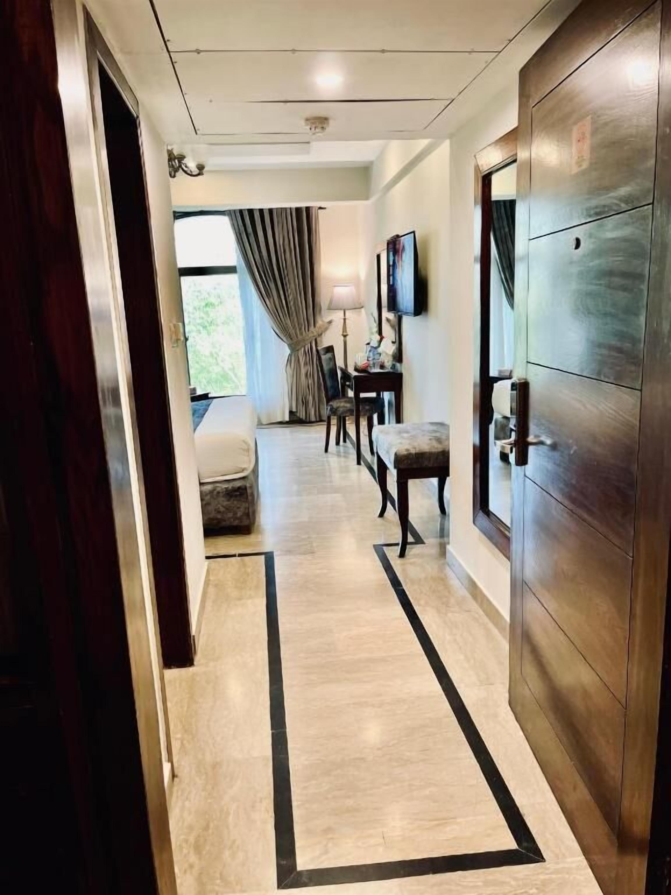 Un pasillo de hotel con una puerta de madera, un comedor con mesa y sillas, y vistas al exterior.