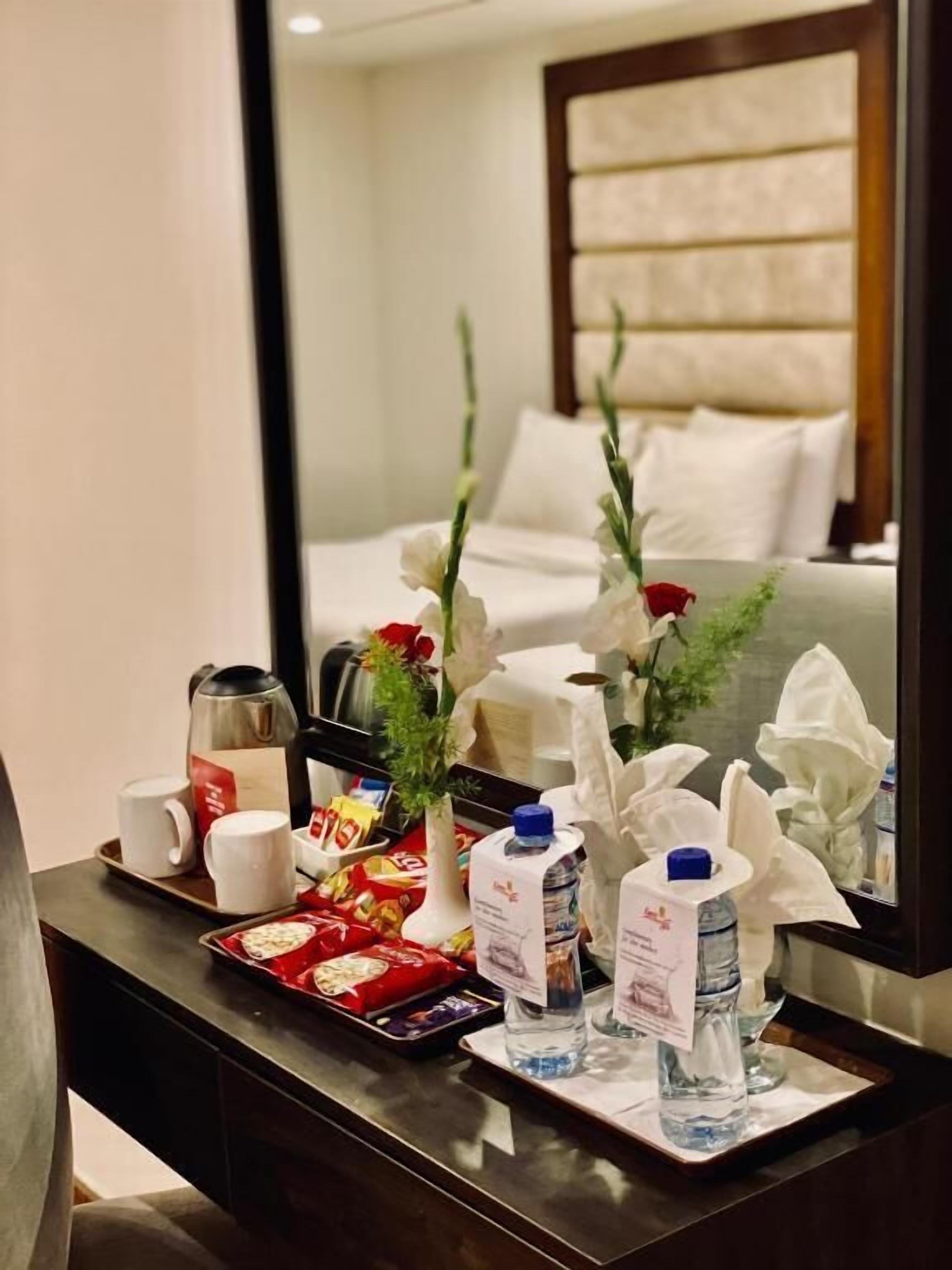 A hotel room with a neatly arranged breakfast tray, including a kettle, cups, a vase with flowers, and bottled water.