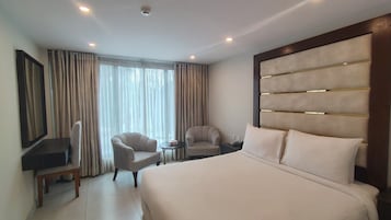 A hotel room with a large bed, two armchairs, a small table, a TV, and a large window with curtains.
