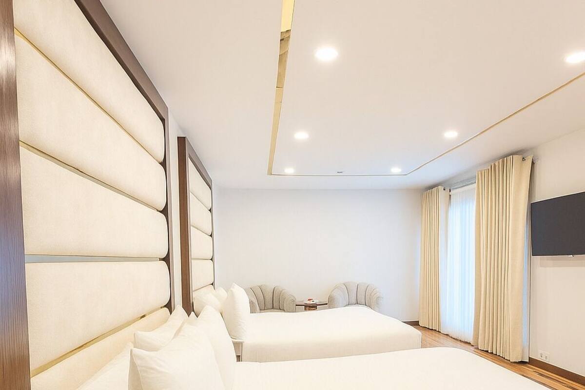 A hotel room with two large beds, a wooden headboard, a flat-screen TV, and a window with curtains.
