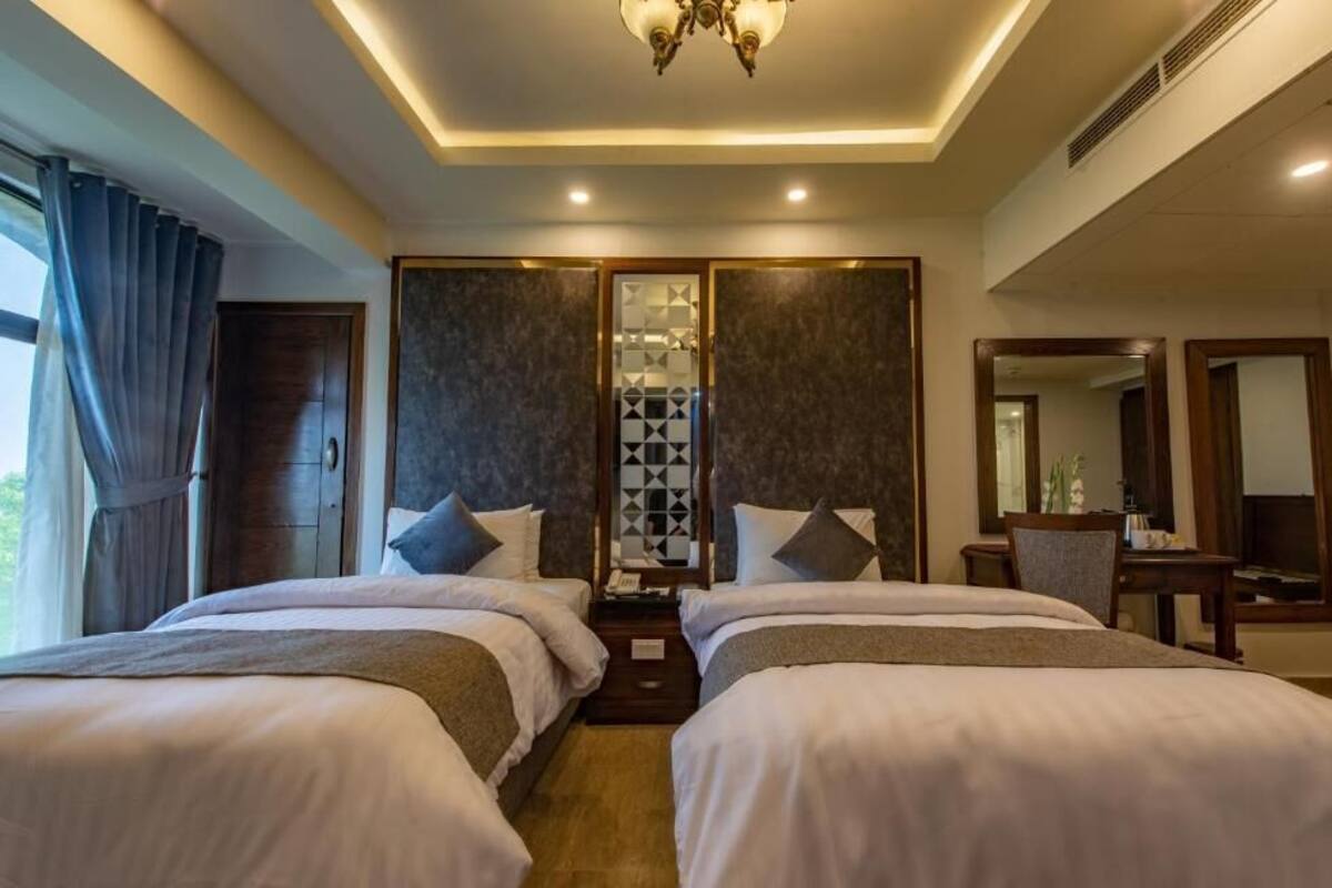 A hotel room with two beds, a large mirror, a desk, and a view of the outdoors.