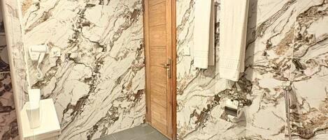 A bathroom with marble walls, a wooden door, a grey floor, a white sink, and a toilet.