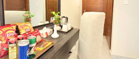 A hotel room with a dark wooden desk, a mirror, a chair, a bed, and a wooden door.