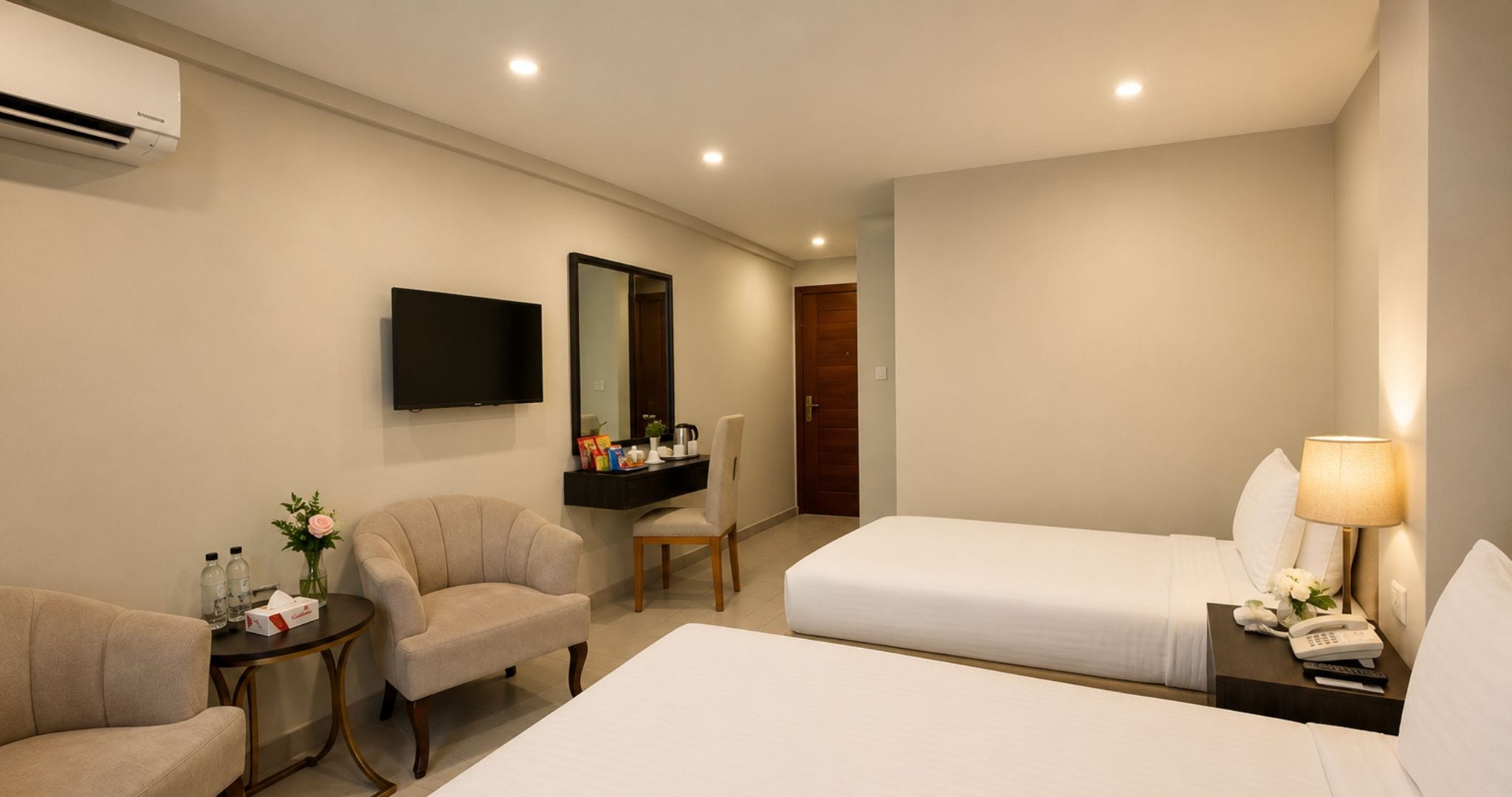 Une chambre d’hôtel avec deux lits, une télévision, un bureau avec une chaise et une table de chevet avec une lampe.