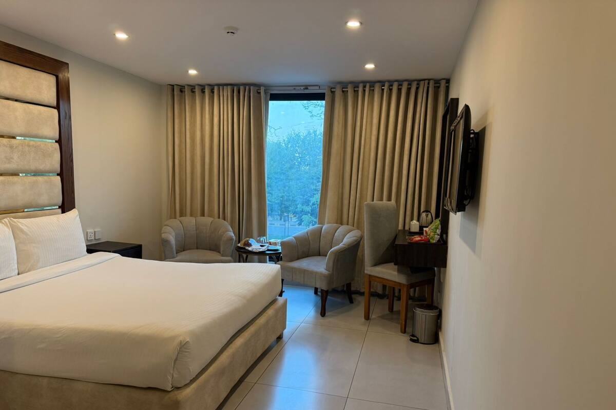 A hotel room with a large bed, two armchairs, a small table, a desk with a lamp, and a TV mounted on the wall.