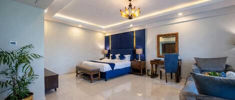 A modern hotel room with a large bed, a desk, a chair, and a potted plant.