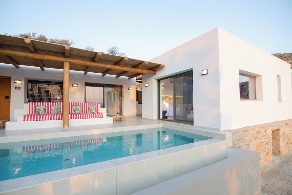 Un área de piscina moderna con una piscina cristalina, una pérgola de madera y un sofá a rayas rojas y blancas con cojines.
