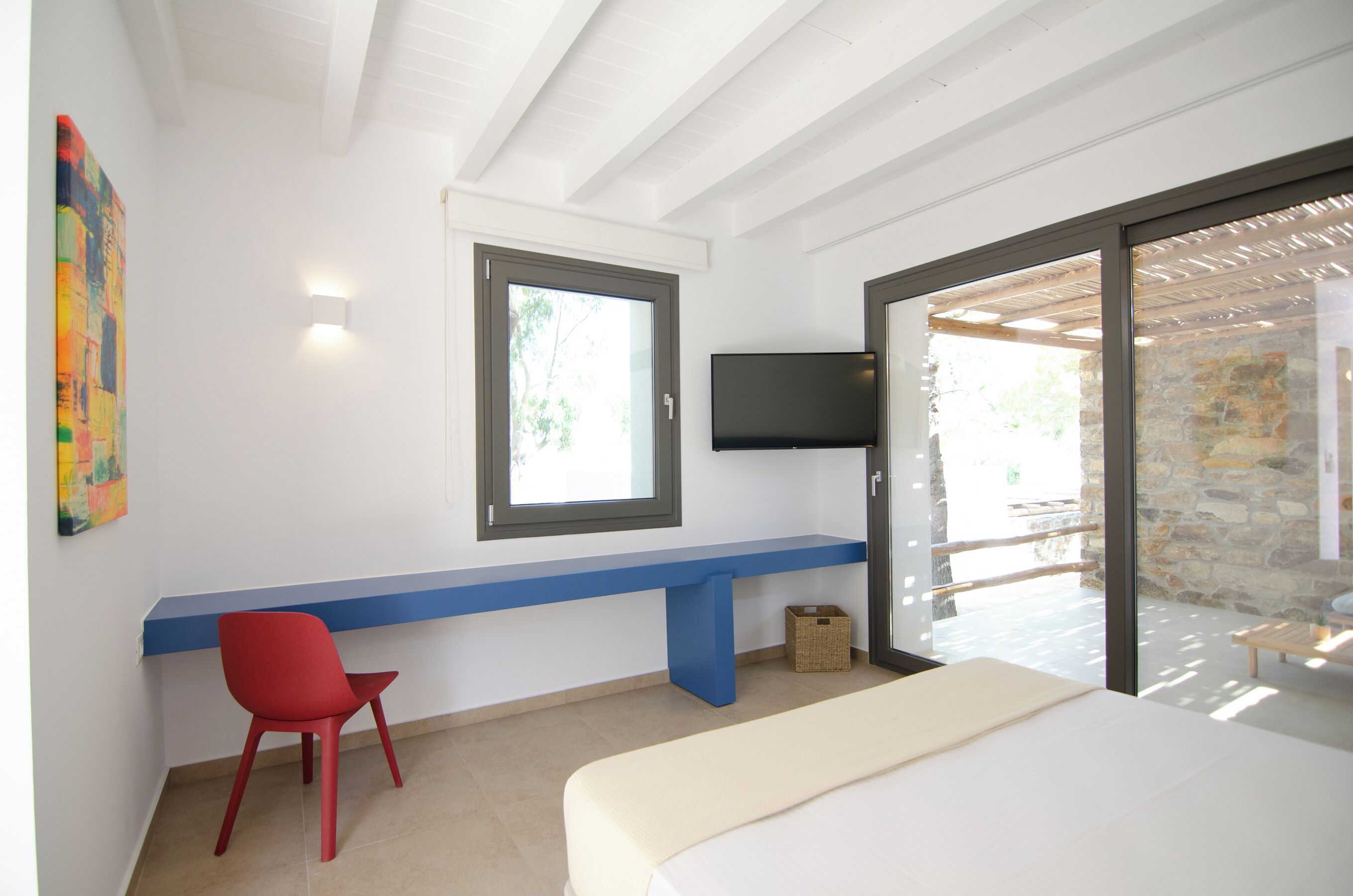 A bedroom with a bed, a red chair, a blue bench, a TV, and a window.
