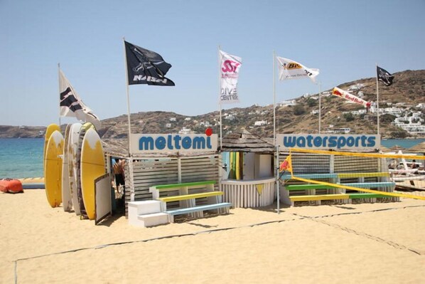 Zona de playa con tablas de surf y una pequeña estructura que indica 'moltemi' y 'deportes acuáticos'.
