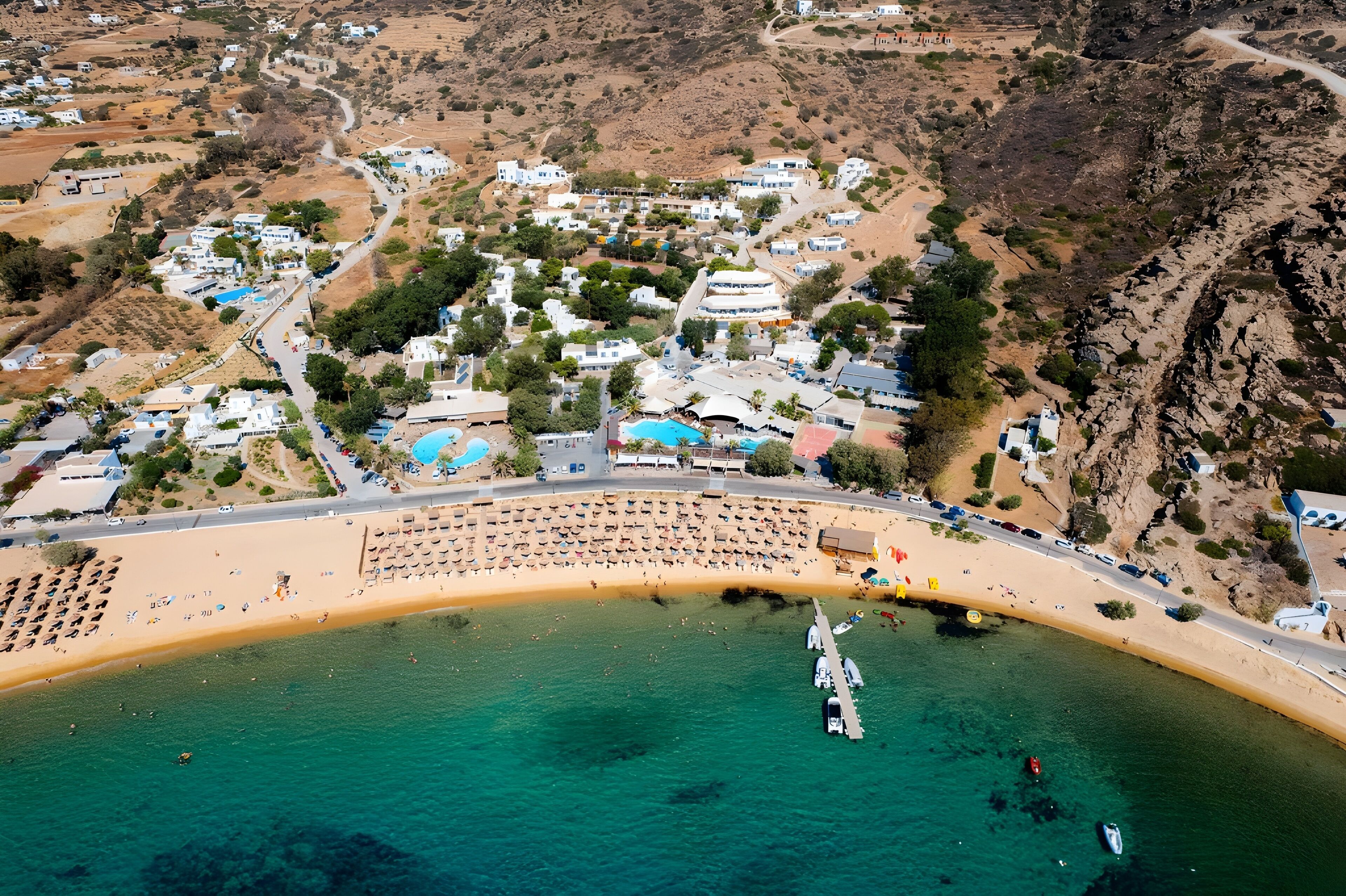 Vista aérea de un pueblo costero con playa, aguas azul cristalino y edificios blancos.
