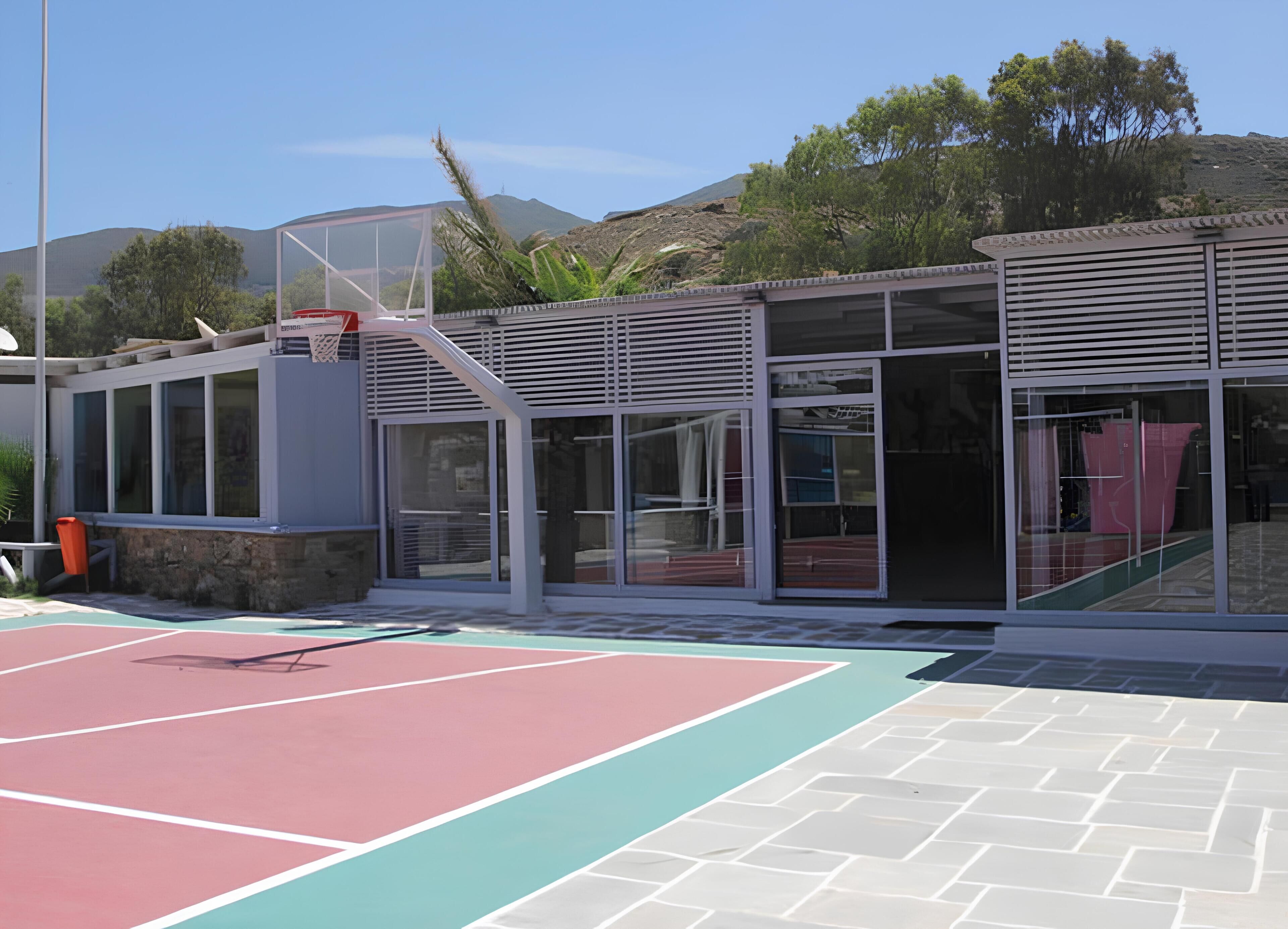 An outdoor basketball court with a modern building featuring large windows and a sloped roof.