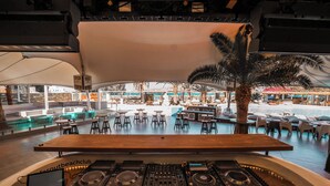 A DJ setup with Pioneer DJ equipment, a pool area with lounge chairs and tables, and a view of the outdoor seating area. - FarOut BeachClub - Rooms & Camping (Ios)
