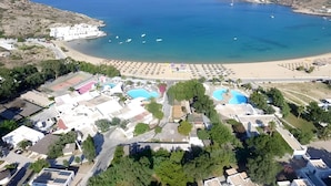An aerial view of a coastal resort with a beach, swimming pools, and a variety of buildings. - FarOut BeachClub - Rooms & Camping (Ios)