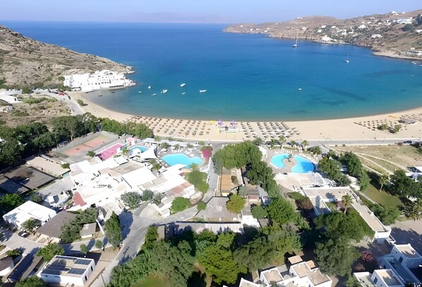 An aerial view of a coastal resort with a beach, swimming pools, and a variety of buildings. - FarOut BeachClub - Rooms & Camping (Ios)