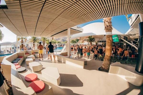A poolside area with lounge seating and a crowd of people. - FarOut BeachClub - Rooms & Camping (Ios)