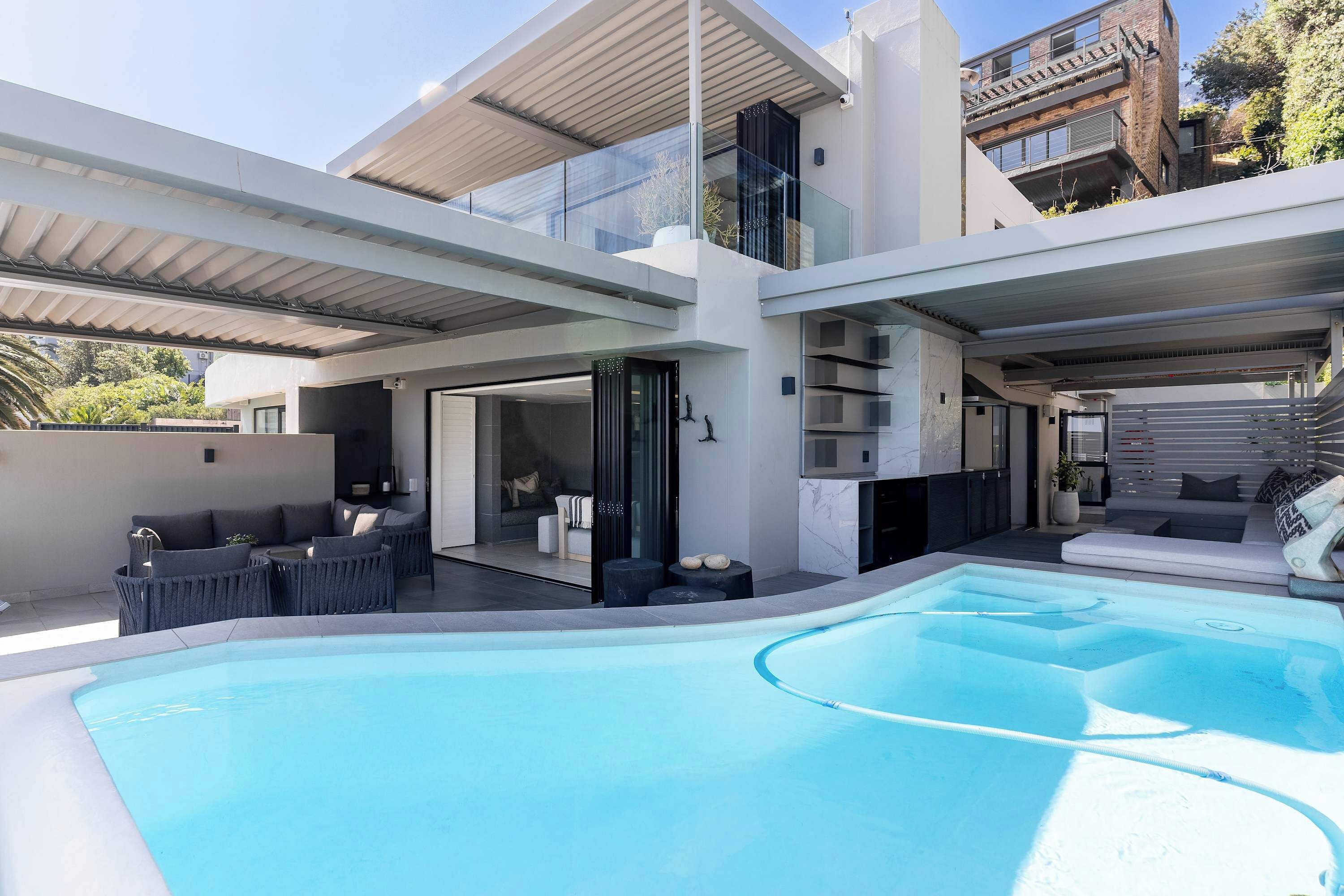 A modern house with a swimming pool, outdoor seating, and a covered patio.