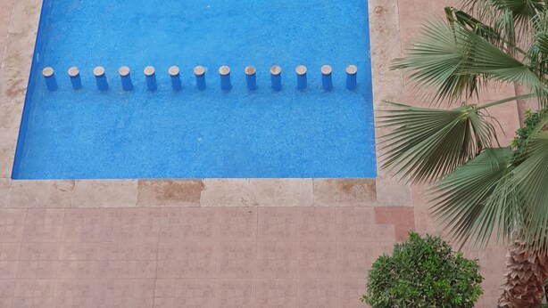 Ein rechteckiger Swimmingpool mit blauer Oberfläche und mehreren zylindrischen Markierungen an einer Seite.