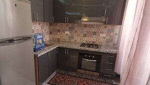 Eine kleine Küche mit dunklen Schränken, einem Edelstahlkühlschrank, einem Gasherd und einem eingebauten Backofen.