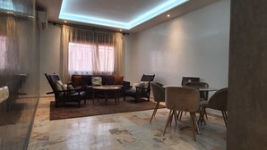 Ein modernes Wohnzimmer mit Marmorboden, einer Sofagarnitur, einem Esstisch mit Stühlen und einer Deckenleuchte.