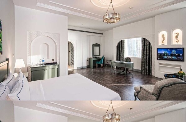 A hotel room with a large bed, a desk, a chair, a television, and a fireplace.