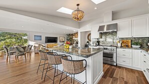 A spacious kitchen with a large island, white cabinetry, and a stone backsplash.