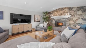 A modern living room with a stone wall, a fireplace, a television, and a comfortable seating area.