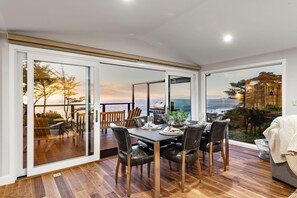 Ein Essbereich mit Meerblick, eine Holzterrasse davor und eine große Schiebeglastür.