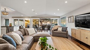 A spacious living area with a large sectional sofa, a coffee table with a plant, a television, and a dining area with chairs and a table.