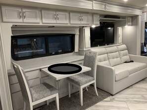 Compact kitchenette with a table, chairs, and bench, featuring a refrigerator and flat-screen TV.