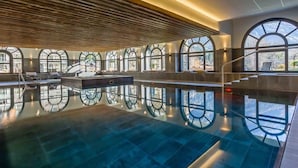 A large indoor swimming pool with arched windows and a wooden ceiling.
