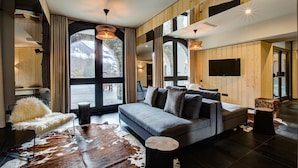 A modern living room with a large sofa, a fur chair, a cowhide rug, and a stone fireplace.