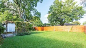 A backyard with a wooden fence, a small shed, and a grassy lawn. - Charming East Dallas Home (Dallas)