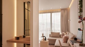A modern living room with a sofa, a desk, and a large window with curtains.