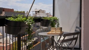 A balcony with potted plants, a table with a tray of glasses, and a chair.