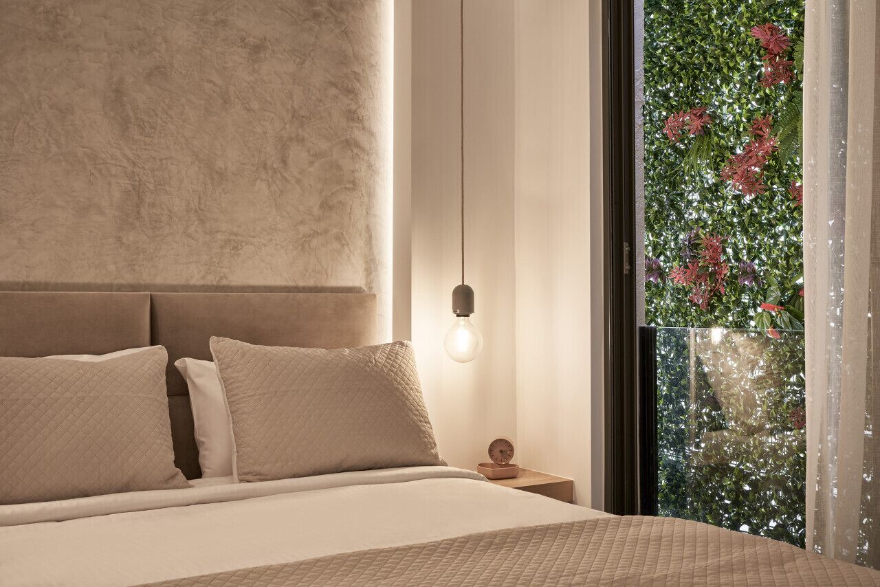 A bedroom with a bed, a nightstand, a wall clock, and a window with a view of greenery.