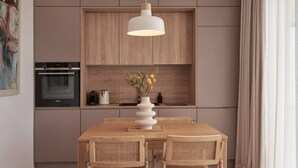 A modern kitchen with wooden cabinets, a built-in oven, a dining table with chairs, and a hanging pendant light.