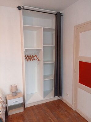 A room with a walk-in closet, a bedside table with a lamp, and a door with a red panel.