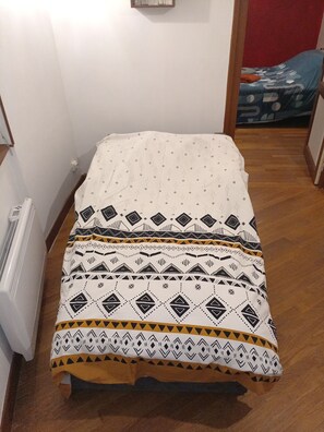 A small room with a bed, a radiator, and a door leading to another room.