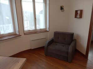 A room with a grey armchair, a radiator, and a window with a view of buildings.