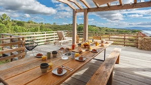 A wooden deck with a breakfast setup including a table, chairs, and a scenic view of the countryside.