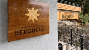 Puinen kyltti, jossa on tähti-aiheinen kuvio ja teksti ”BERGQUELL”, on kiinnitetty valkoiseen seinään.