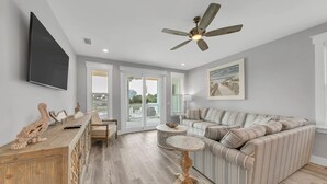 A modern living room with a sectional sofa, a wooden coffee table, and a ceiling fan. - Surf-N-Santa, 6 BR/4 BA, Private Pool with Hot Tub, West End PCB, Sleeps 18 (Panama City Beach)