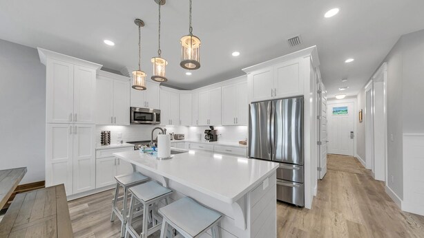 A modern kitchen with white cabinetry, stainless steel appliances, and a central island with bar stools. - Surf-N-Santa, 6 BR/4 BA, Private Pool with Hot Tub, West End PCB, Sleeps 18 (Panama City Beach)