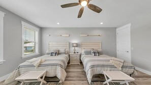 Quarto com duas camas, um ventilador de teto, mesas de cabeceira e uma janela com persianas.