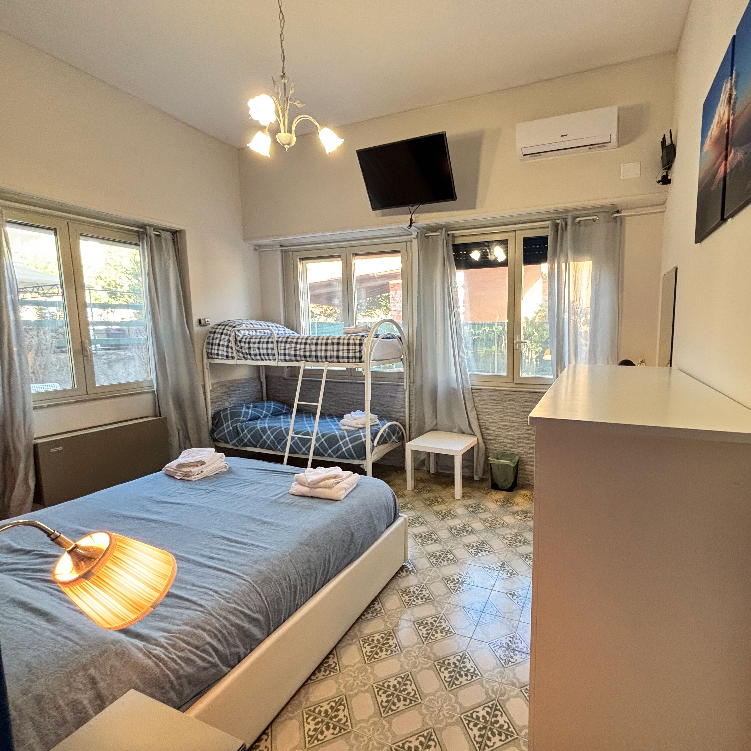 A bedroom with a bunk bed, a desk, a chair, a TV, and a window with curtains.