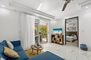 Relax in this stylish living room with a sofa, coffee table, and sliding door to an outdoor area with a view of lush greenery.
