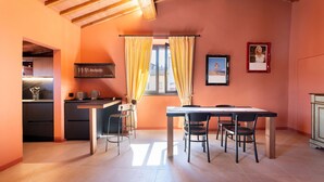 Une cuisine compacte avec un coin repas, dotée d’un plafond en bois, d’une fenêtre avec des rideaux jaunes et d’une petite table à manger avec des chaises.