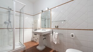 A bathroom with a glass-enclosed shower, a pedestal sink, a mirror, and a toilet.